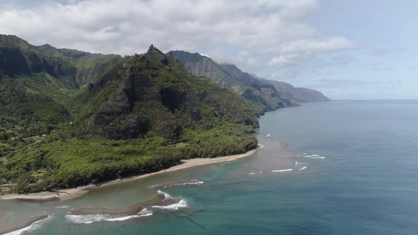 Clear ocean water meets with a white sandy beach and lush tropical forest and mountains