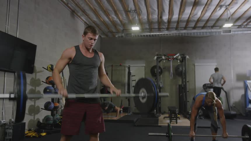 A squatting man lifts up a barbell and then drops it to the floor