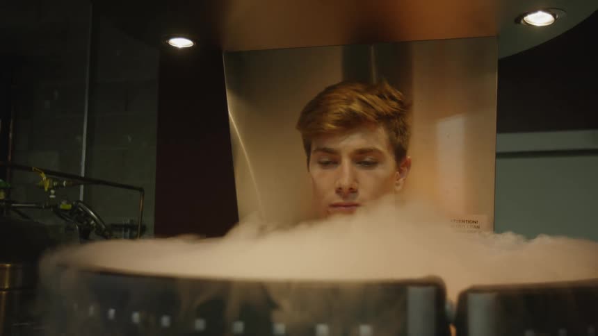 A man stands in a large cryotherapy cylinder with smoke pouring out the top