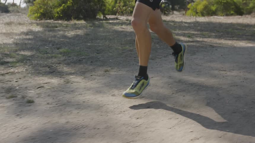 A shot of legs of a man running on the sand with sneakers