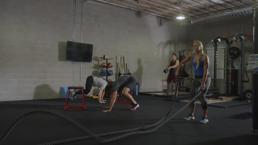 Female doing battle ropes while guys workout behind her at the gym