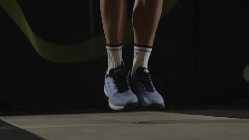 Man wearing light blue trainers jumps yellow rope on the black background