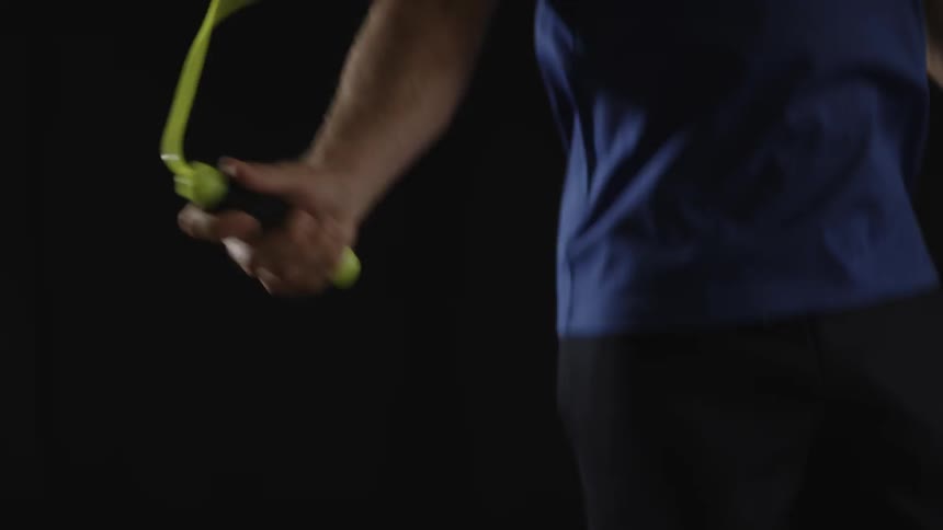Man in a dark room is jumping rope with a neon yellow jump rope