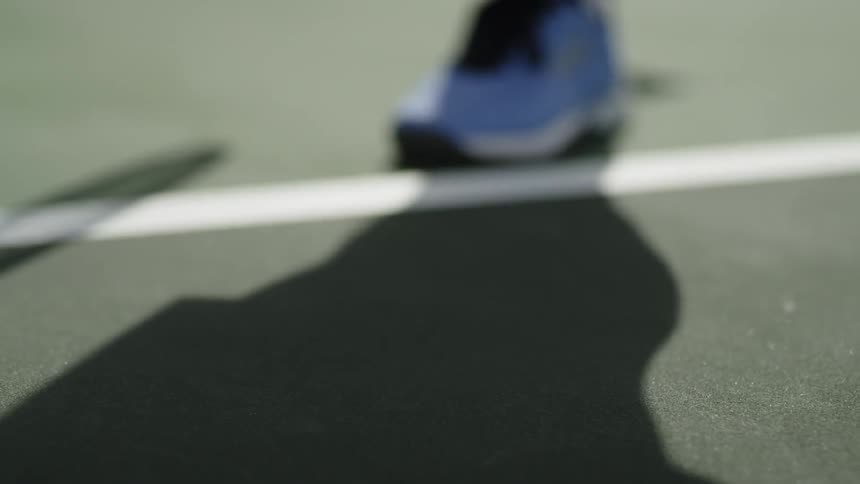 Yellow tennis ball bouncing on court near blue tennis shoes