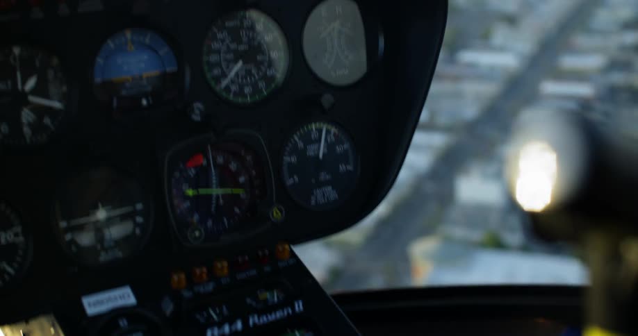The control panel of a helicopter is shown as it flies over a city