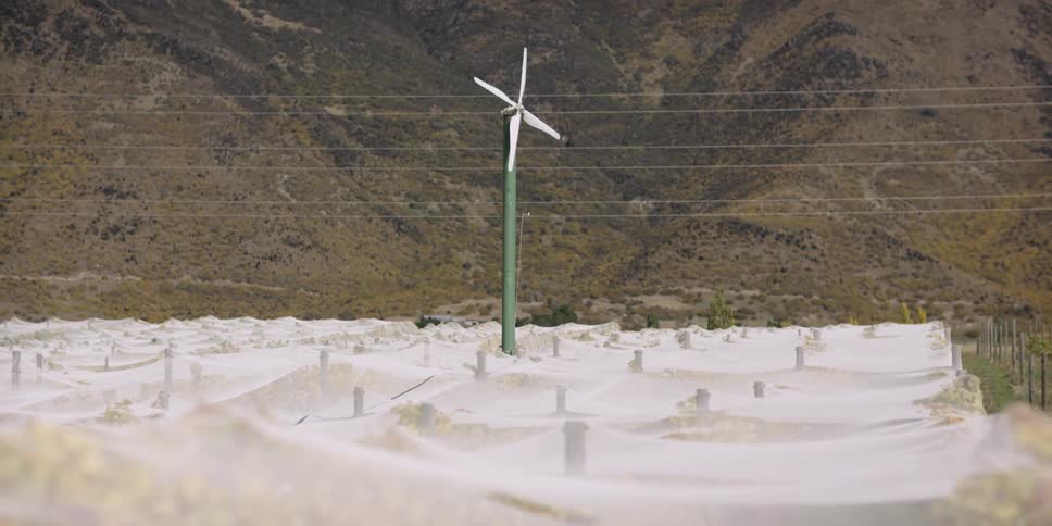 A wind turbine sits on a large field with mountains in the distance