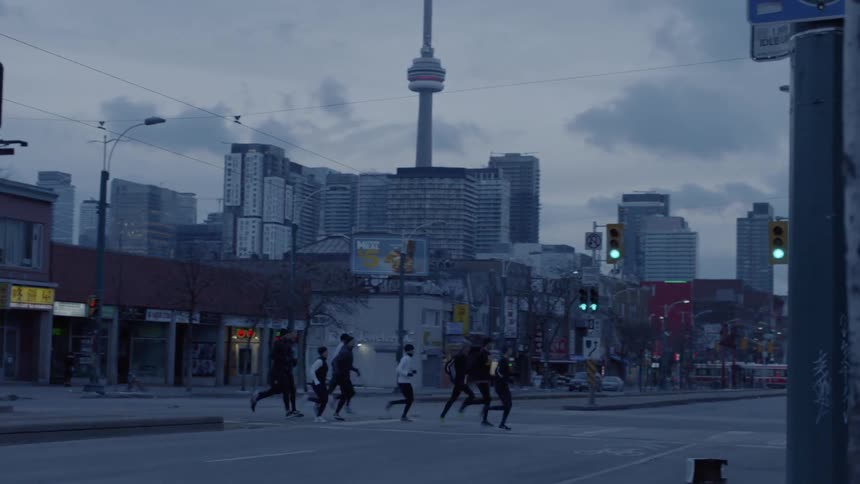 A group of runner that are dressed for cold weather jog across the crosswalk of an urban street in a large city