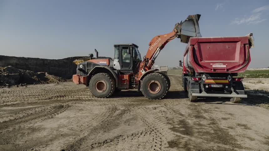 Construction vehicles pick up dirt and put it other vehicles that drive away