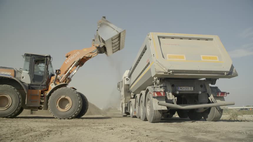 A loader empties into a dump truck and then backs away