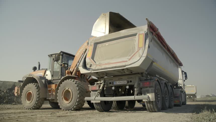 A tractor scoops up dirt and drops it into a dump truck
