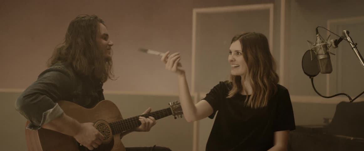 A man and a woman are writing a song as the woman works out the notes and the man plays guitar
