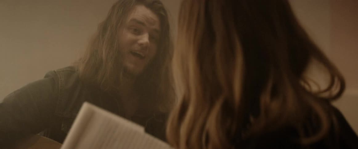 A man and a woman write a song together as the man plays guitar and the woman writes lyrics