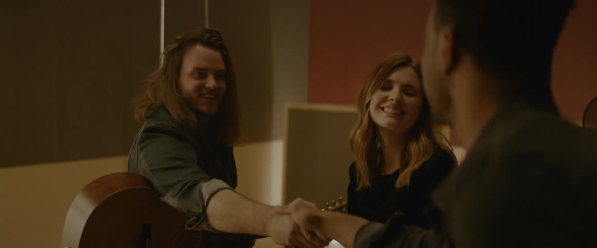 Long hair man plays a guitar and woman sings indoors
