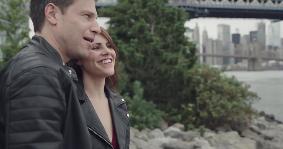 A man and woman are talking to each other in a park near a bridge