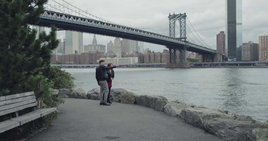 A man and woman stand on a path by the city harbor and take a selfie