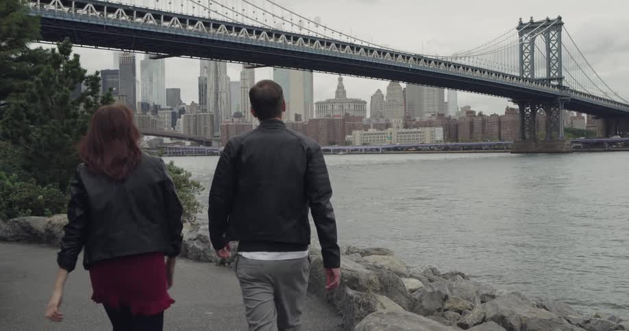 People walk along a body of water near a bridge