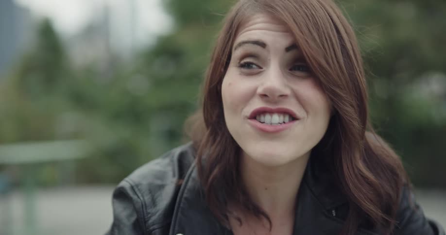 Woman wearing black leather jacket talks and smiles in the public park on a cloudy day