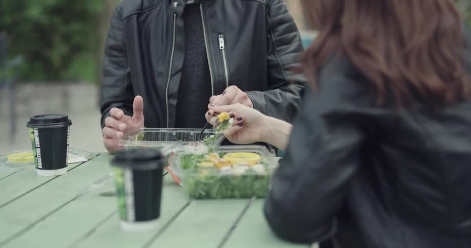 Man and woman eat prepackaged salads at an outside table