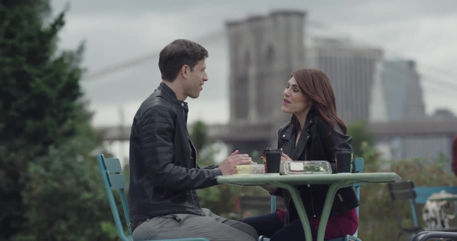 A man and a woman sit at a table talking and eating