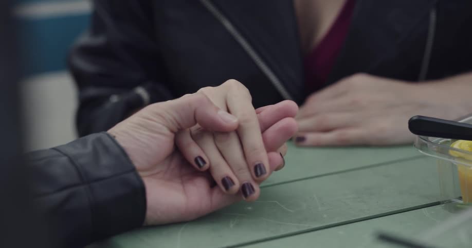 A man and woman sit at a table holding hands