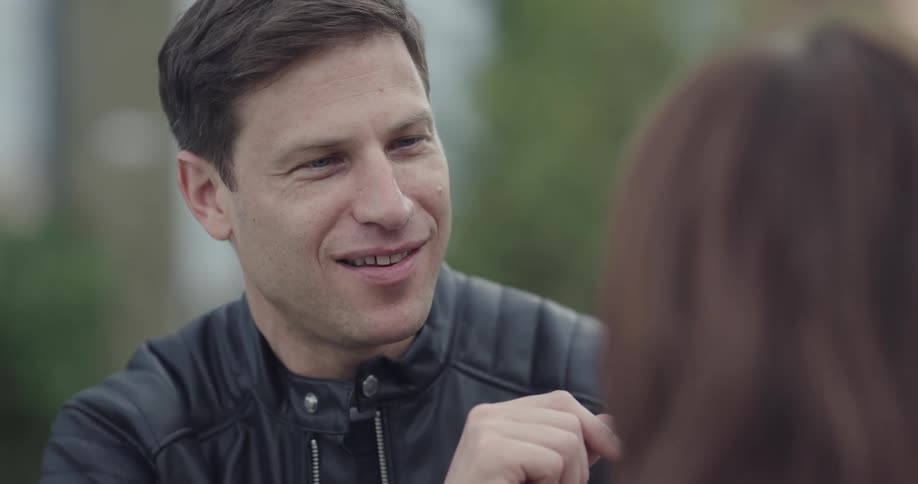 Man wearing black leather jacket talks to woman and smiles on a cloudy day
