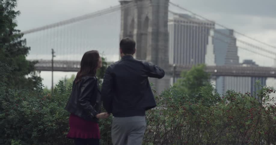 People walk into an area in front of a suspension bridge with an american flag atop the support column