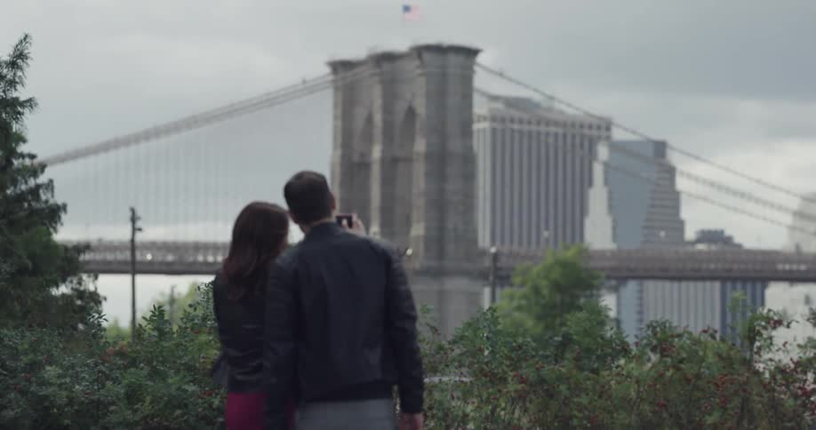 Couple take photo outdoors with suspension bridge in background
