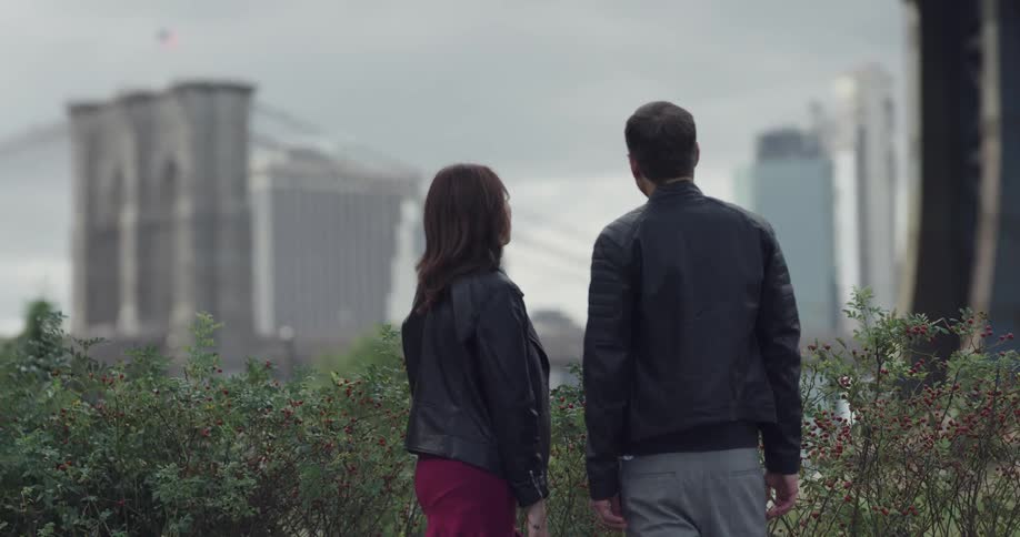 A man and woman stand outside in a city and chat