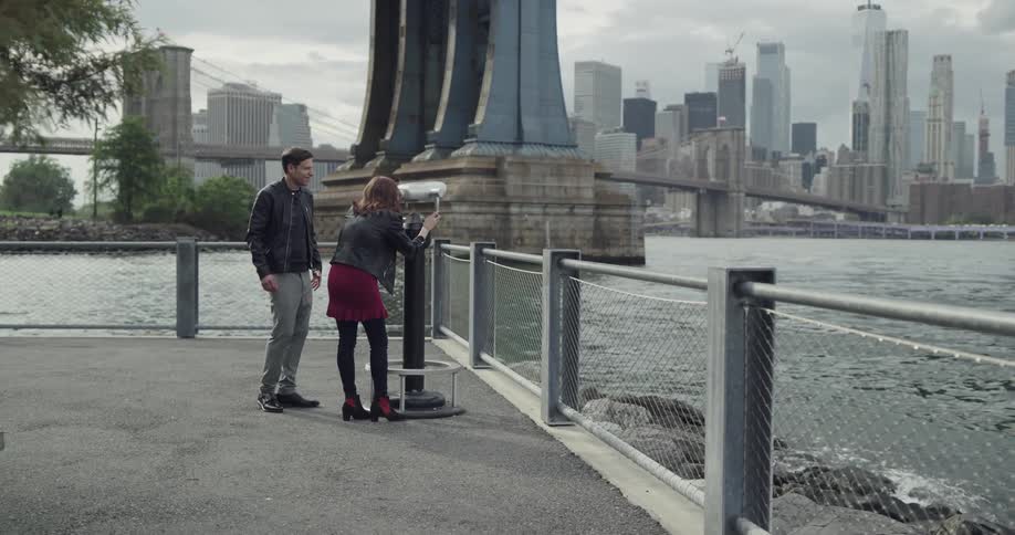 A man and woman stare through public binoculars in a park across from new york city