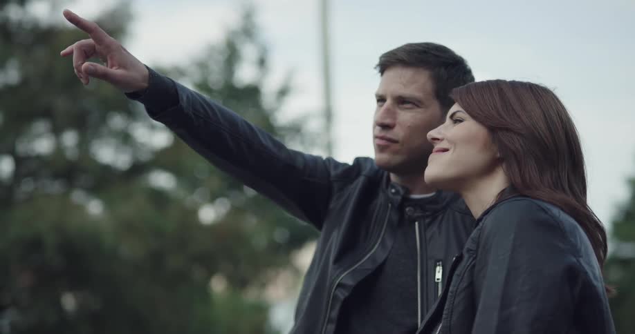 A man and a woman in leather jackets discuss something off screen