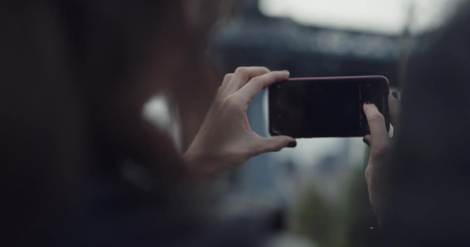 A woman raises her cell phone to take a picture of the bridge in front of her