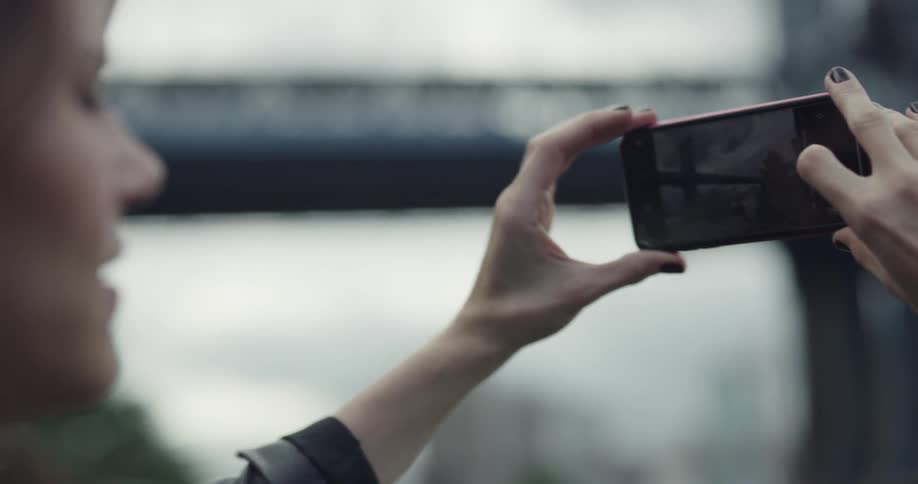 Woman takes a picture of the bridge with a smartphone on a cloudy day