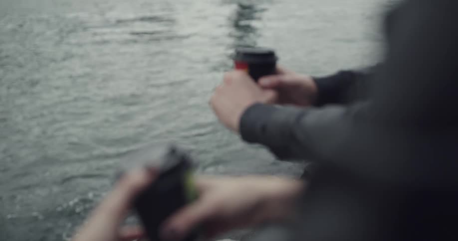 A man and a woman are each holding a cup next to some water