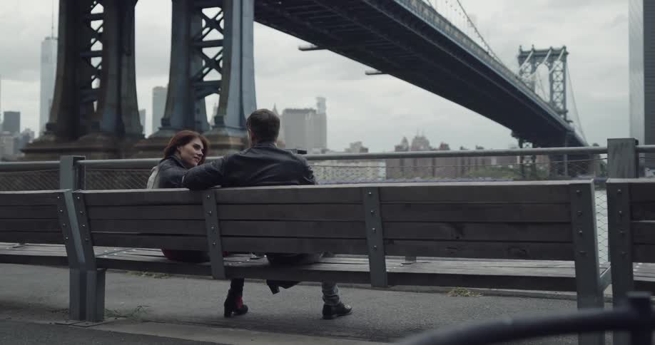 A couple cuddling romantically on the park bench under brooklyn bridge