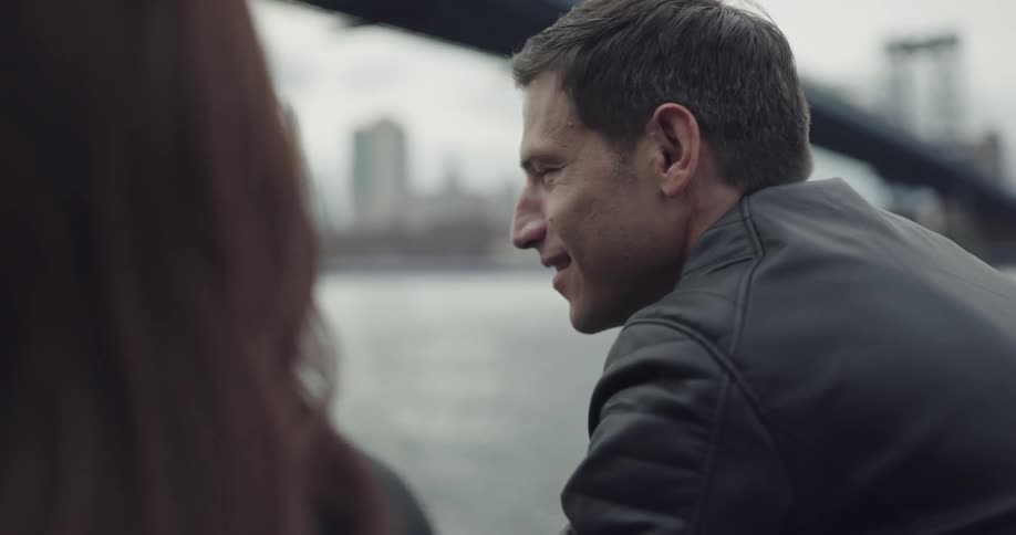 Man wearing black leather jacket talks to the woman by the sea on a cloudy day