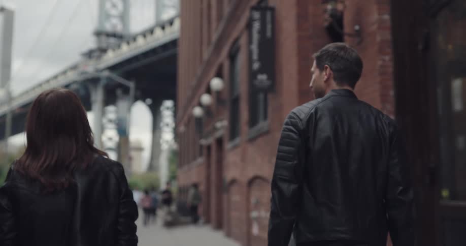 Couple wearing leather jackets walking in the city towards a bridge