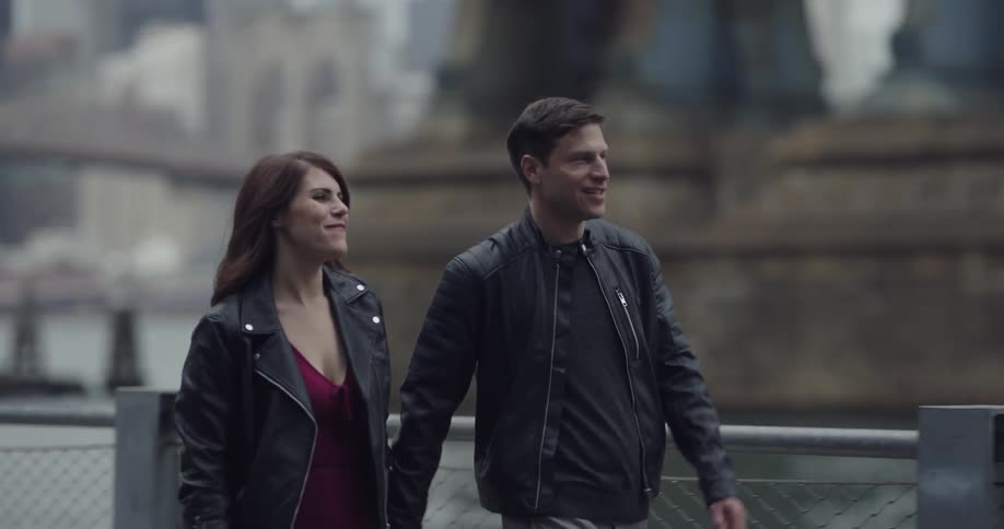 Man and woman wearing black leather jackets date by the sea side across the city on a cloudy day