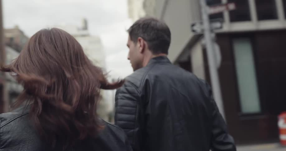 Man and woman in black leather jackets walk down the street in the city during daylight