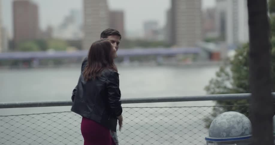 A man greets a woman with a kiss and they walk off holding hands