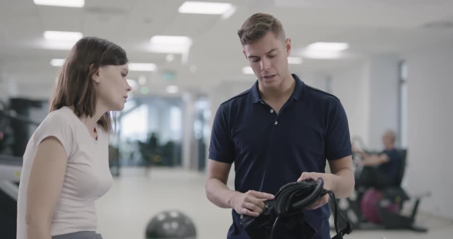 A gym instructor give some instruction to a female on the gym