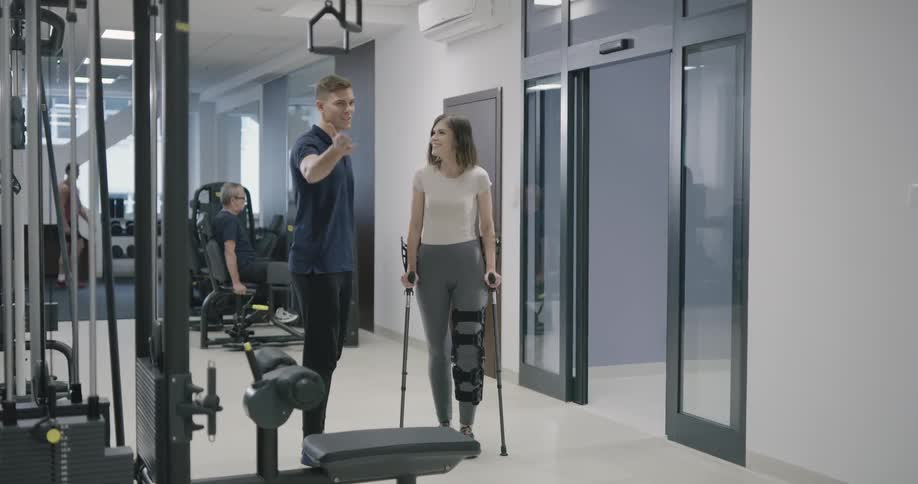 A woman uses crutches to walk into a room and is greeted by a man