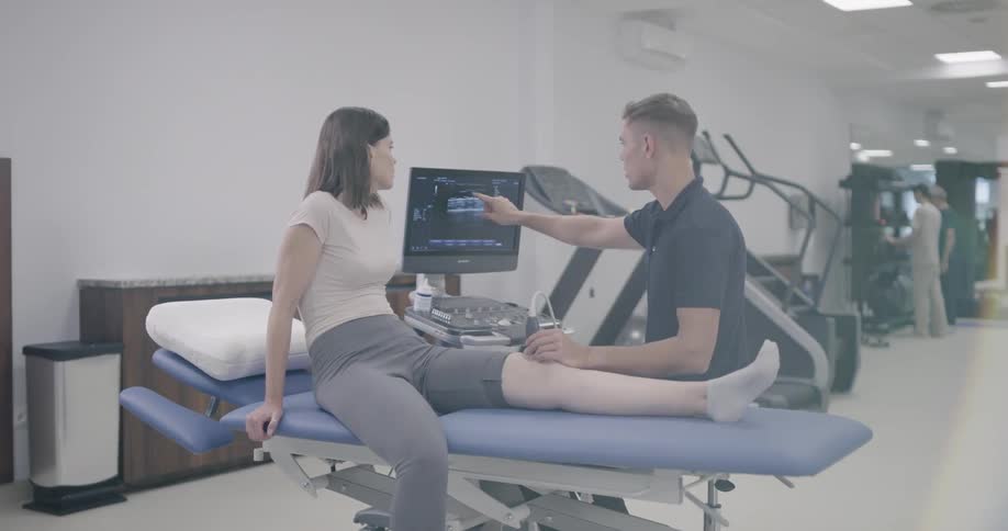 A young man holds a scope on a womans knee and looks at a computer screen