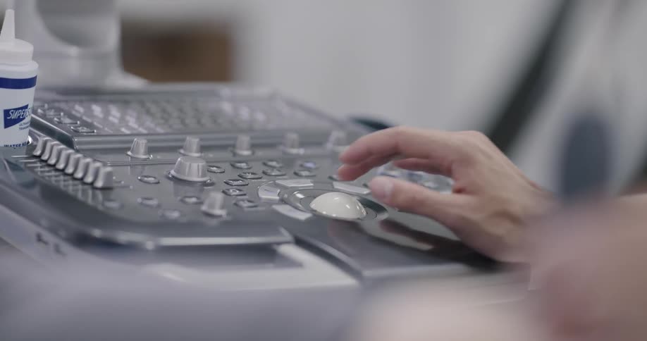 A medical professional adjusts multiple knobs on an ultrasound machine control panel