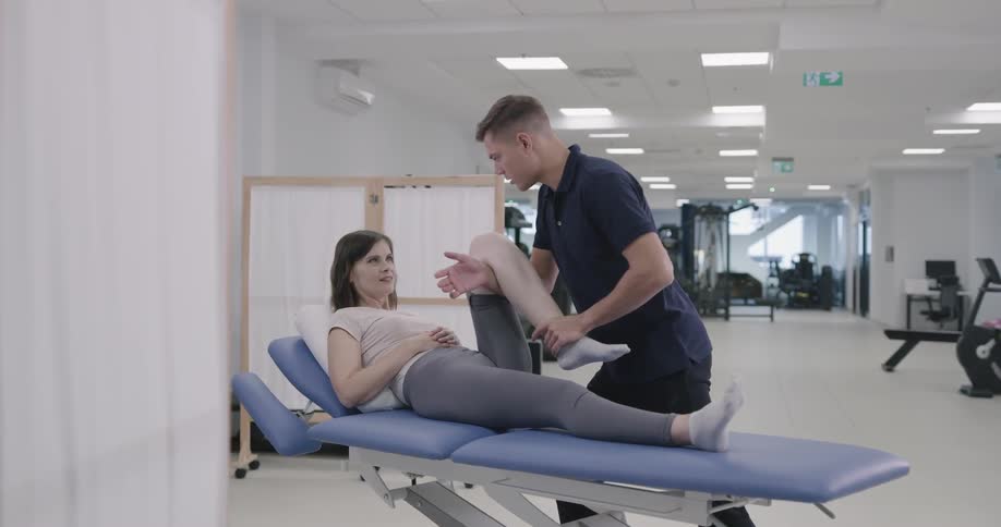 A physical therapist helps a patient flex her knee while reclined on a bed