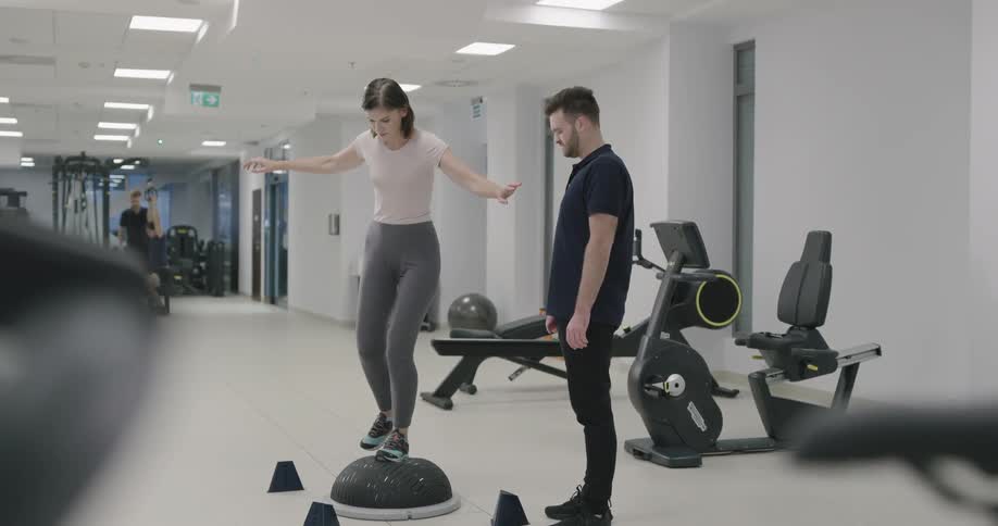 Woman balances on cushion under guidance of trainer
