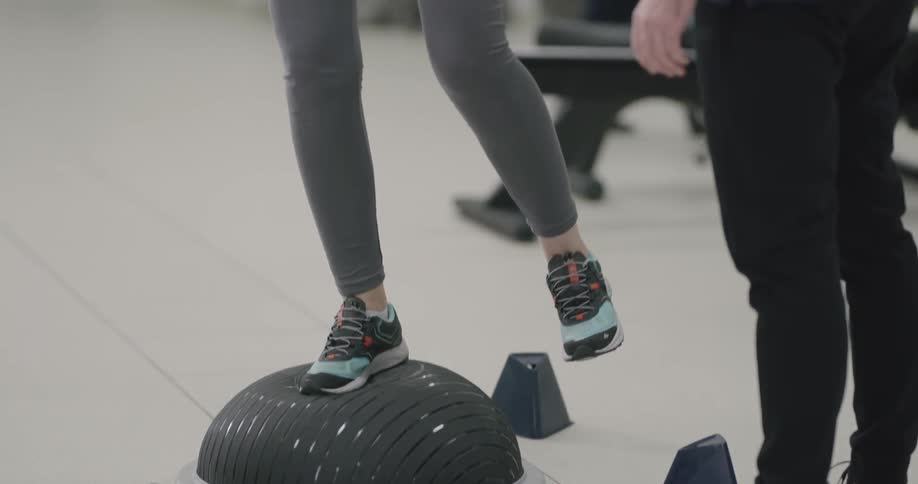 Female standing on a half sphere shaped device to train her balance