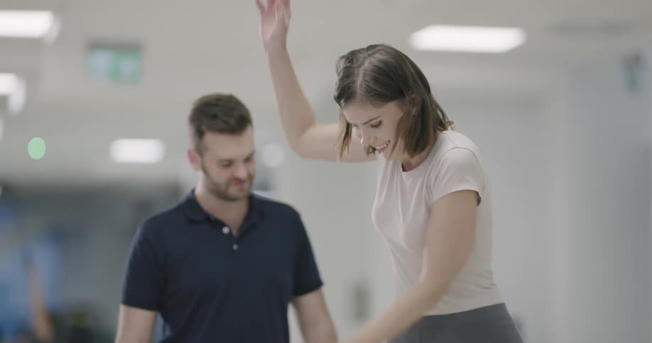 A woman doing balance exercises under the guidance of personal trainer in a fitness clinic
