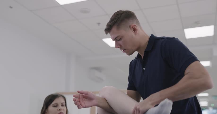 A man performs physical therapy exercises on a woman