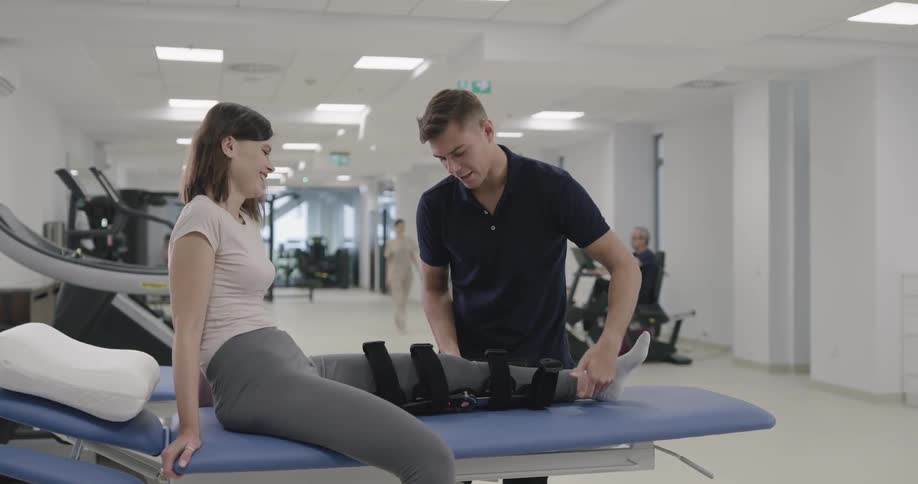A physical therapist takes a brace off a womans leg