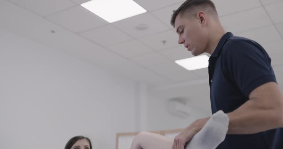 A woman in physical therapy getting her leg stretched by a man